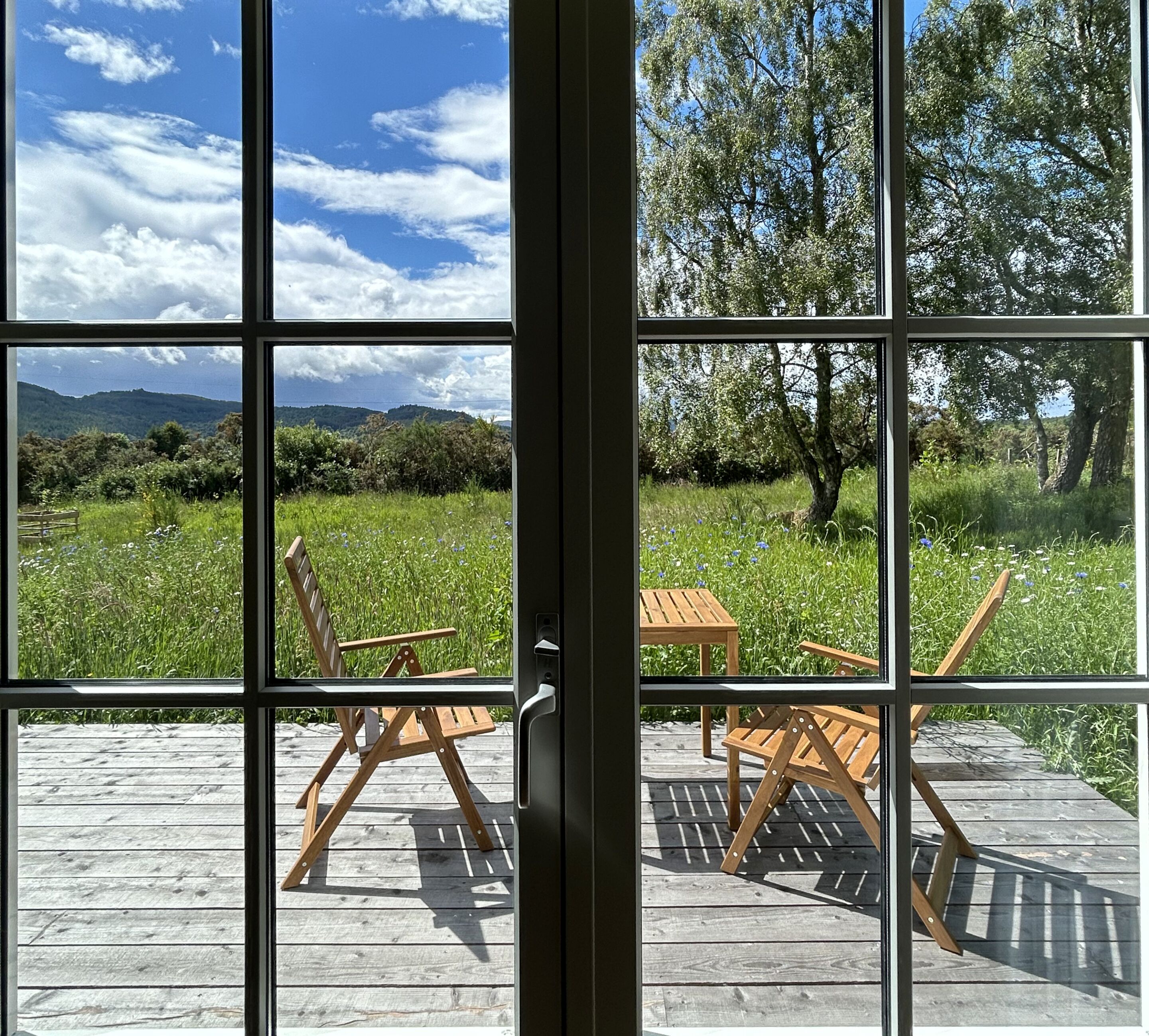 View from No. 2; private deck with outdoor dining, overlooking birches, wildflowers, and rolling hills.