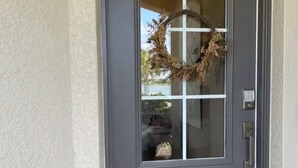 Una puerta principal gris oscuro con un panel de vidrio y una corona.