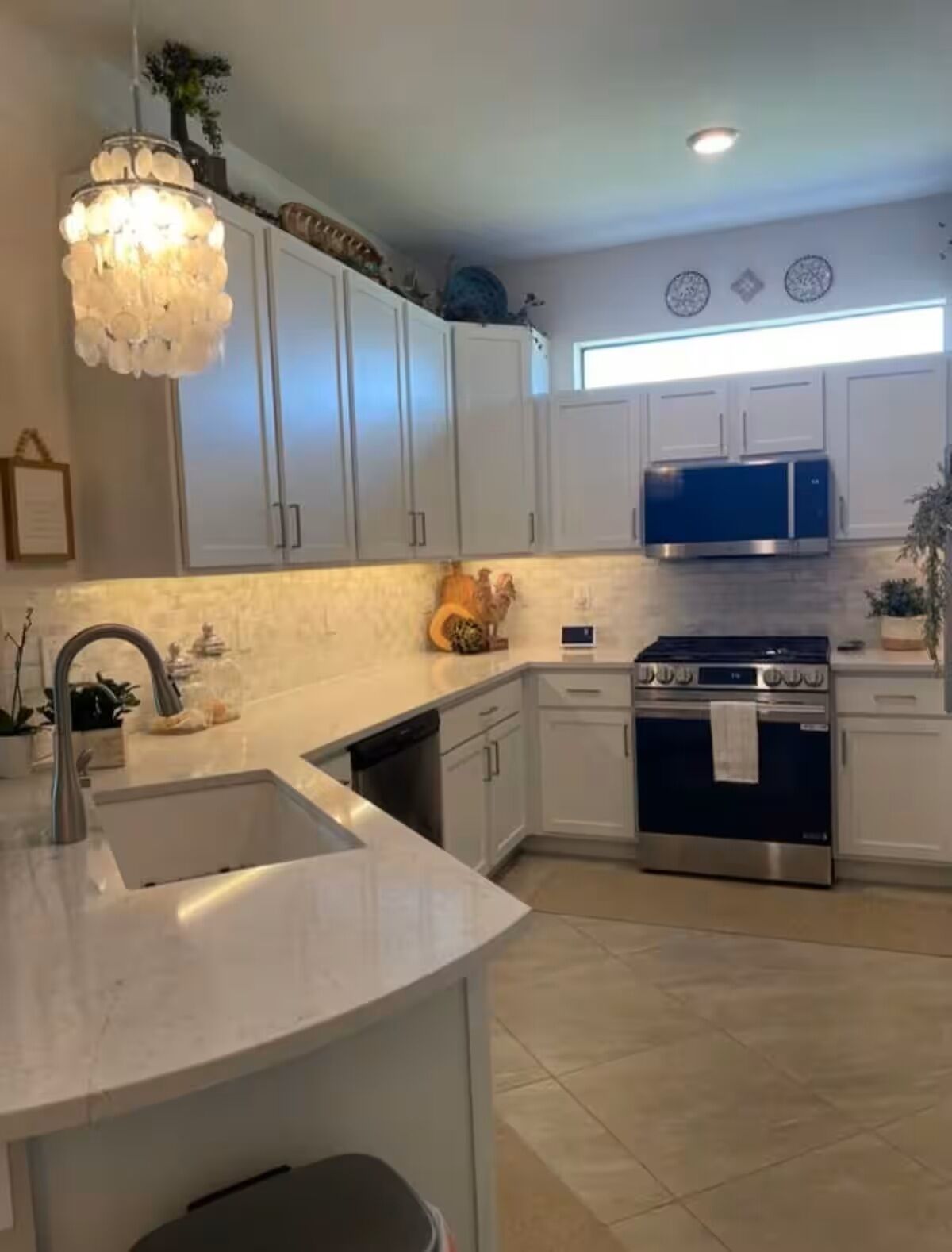 A kitchen with white cabinets, a stainless steel sink, a blue microwave, and a gas stove.