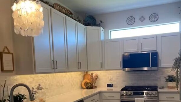 Una cocina con armarios blancos, un lavamanos de acero inoxidable, un microondas azul y una estufa a gas.