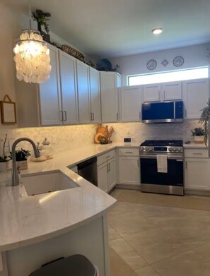 A kitchen with white cabinets, a stainless steel sink, a blue microwave, and a gas stove. - Charming 2-bedroom Villa on water w/ Many Amenities in gated Lakewood Ranch (Bradenton)