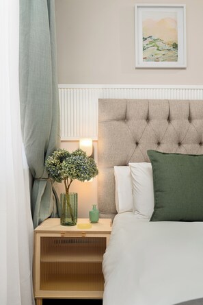 A neatly made bed with a tufted headboard, a bedside table with a vase and a lamp, and a framed picture on the wall. - Charlie and the Chairman Modern CBD Retreat (Cape Town)