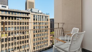 Un balcon avec deux chaises blanches, une vue sur un immeuble portant l’inscription « LUNO », et un ciel dégagé.