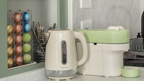 Une cuisine équipée d’une bouilloire, d’une machine à café et de récipients de rangement étiquetés « SUCRE », « THÉ » et « CAFÉ ».