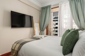 A hotel room with a bed, a flat-screen TV mounted on the wall, a window with curtains, and a view of the outside. - Charlie and the Chairman Modern CBD Retreat (Cape Town)