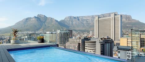 A rooftop pool with a cityscape and mountains in the background.
