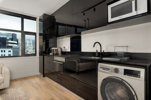 A modern kitchen with a built-in washer and dryer, stainless steel appliances, and a view of the city through a large window. - The Tokyo | Rooftop Pool | No Loadshedding (Cape Town)