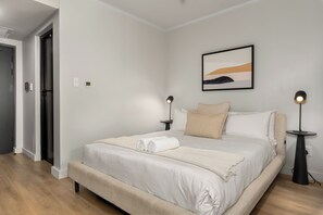 A hotel room with a bed, bedside tables, a painting, and a door. - The Tokyo | Rooftop Pool | No Loadshedding (Cape Town)