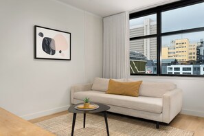 A modern living room with a sofa, a small table, and a city view through large windows. - The Tokyo | Rooftop Pool | No Loadshedding (Cape Town)