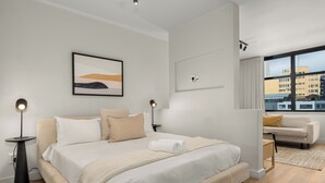 Ett modernt hotellrum med en stor säng, sängbord, en soffa och utsikt över staden.