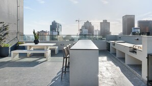 En takterrass med ett långt bord, bänkar och en bar.
