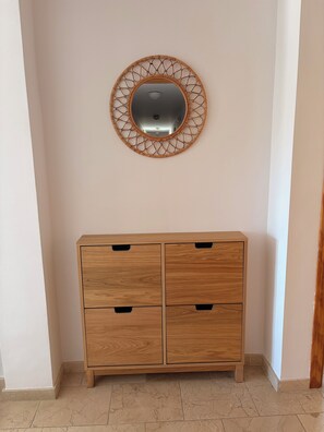 Eine Holzkabine mit vier Schubladen und ein runder Spiegel mit geometrischem Rahmen an der Wand.