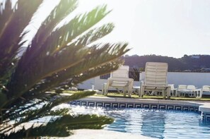 Ein Poolbereich mit Liegestühlen und Blick auf eine entfernte Landschaft.
