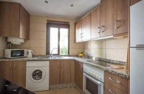 A compact kitchen with wooden cabinets, a built-in washing machine, a microwave, and a stove. - 3 bedroom, central apartment with communal pool and stunning views (Frigiliana)