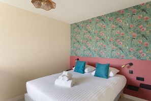 Ein Hotelzimmer mit einem Bett, zwei Kissen, einer Wandlampe und einer Wand mit Blumenwallpaper.