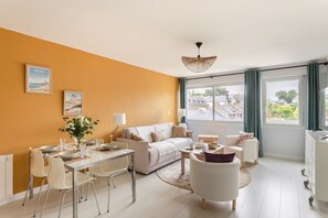 Ein modernes Wohnzimmer mit einer Couch, einem Esstisch, Stühlen und Blick auf die Stadt durch große Fenster.