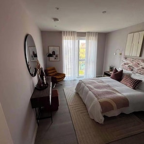 Een slaapkamer met een bed, een bureau, een stoel, een spiegel en een raam met gordijnen.