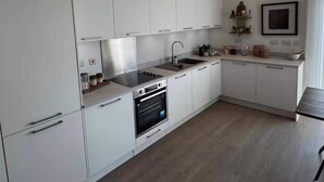 A modern kitchen with white cabinets, a built-in oven, and a stainless steel sink. - Cozy London Apartment With 2 Bedrooms (London)