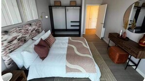 A bedroom with a bed, bedside table, dresser, mirror, wardrobe, and a door leading to another room. - Cozy London Apartment With 2 Bedrooms (London)