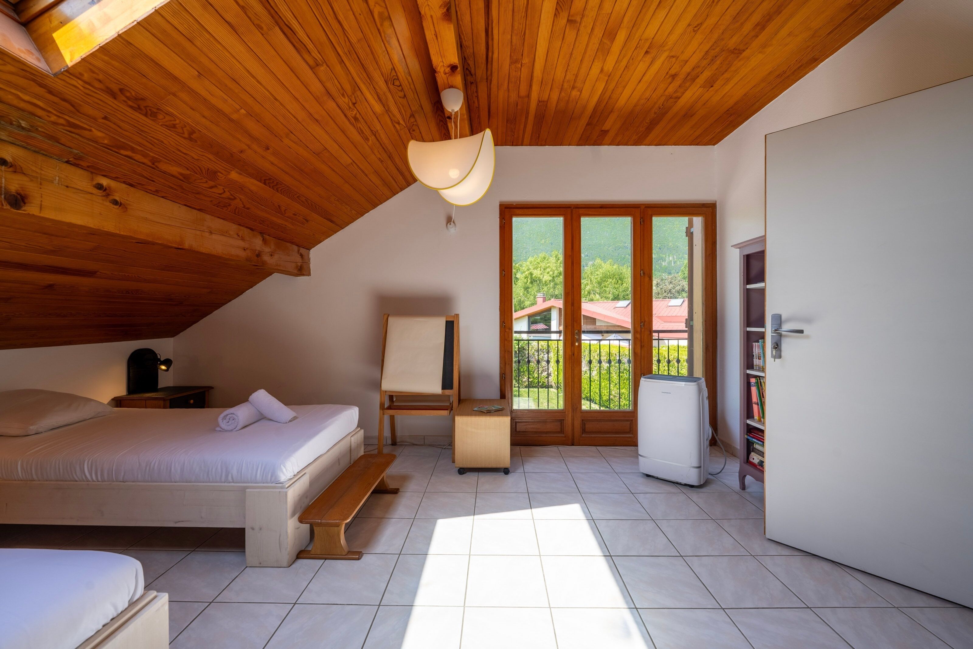 A bedroom with a bed, a desk, a chair, a wardrobe, and a view of the outside.