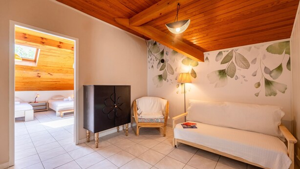 Ein gemütliches Zimmer mit Holzbalkendecke, einer Couch, einem Sessel, einem Fernseher und einer Wand mit Blattmuster.