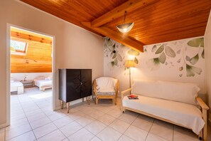 Ein gemütliches Zimmer mit Holzbalkendecke, einer Couch, einem Sessel, einem Fernseher und einer Wand mit Blattmuster.