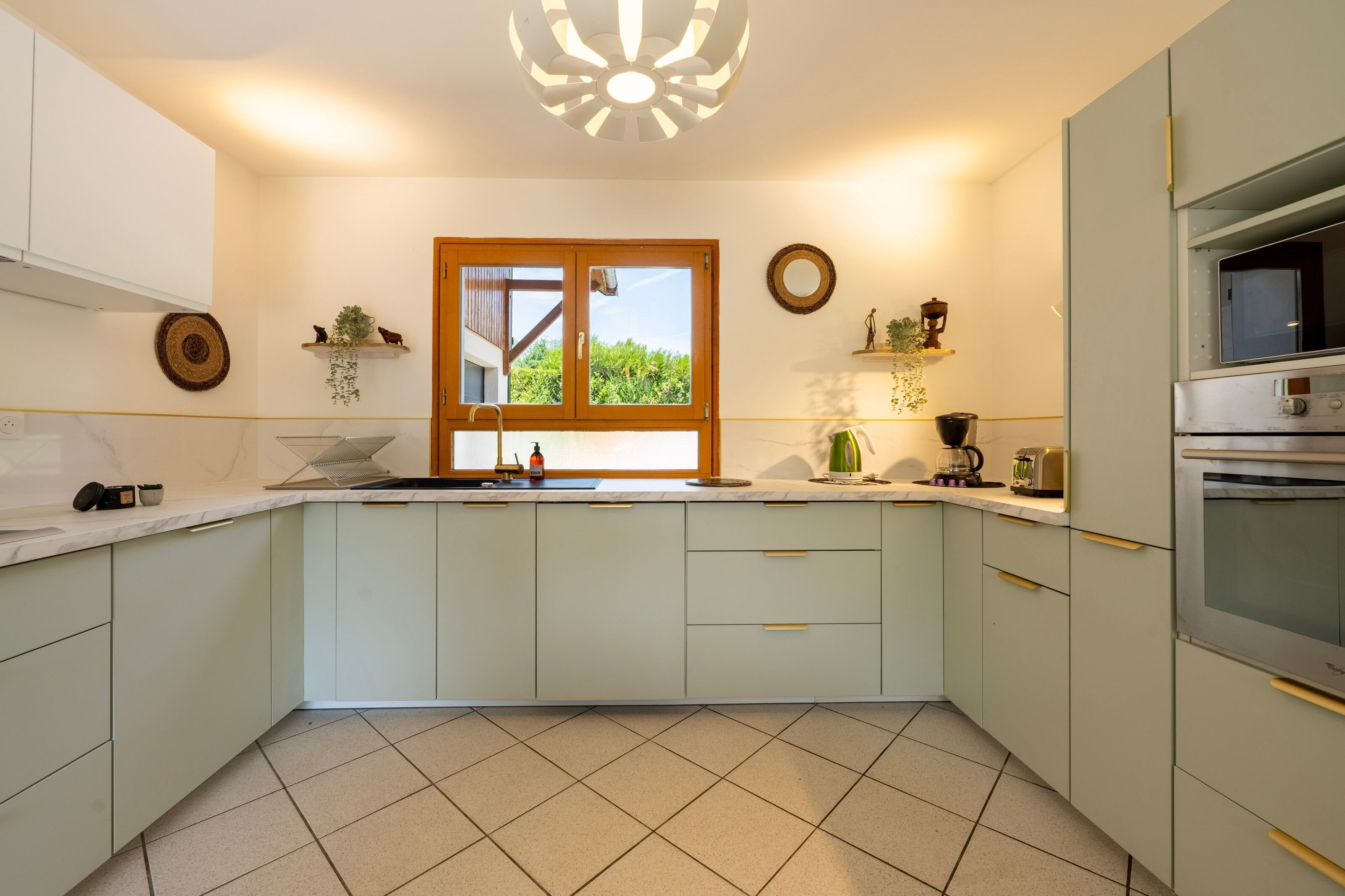 A modern kitchen with a window, white cabinets, and a tiled floor.