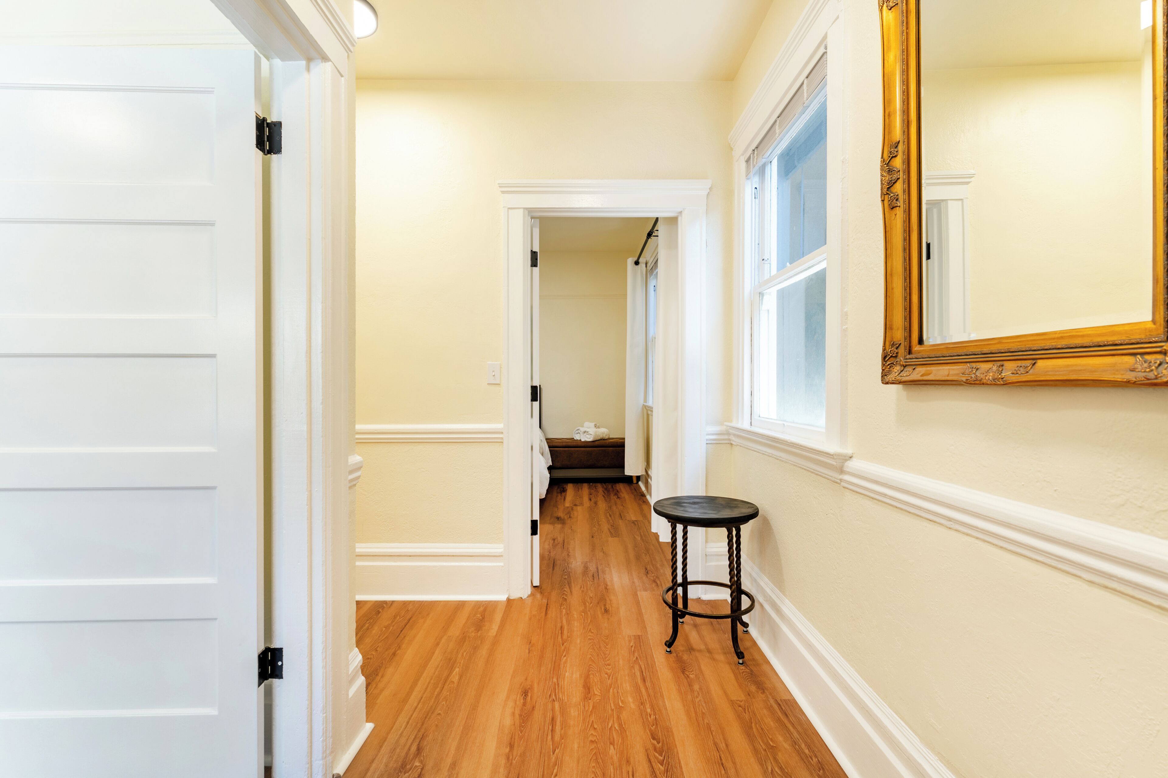 A hallway with wooden flooring, a white door, a black round table, and a large mirror on the wall.