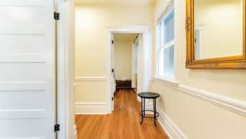 A hallway with wooden flooring, a white door, a black round table, and a large mirror on the wall.