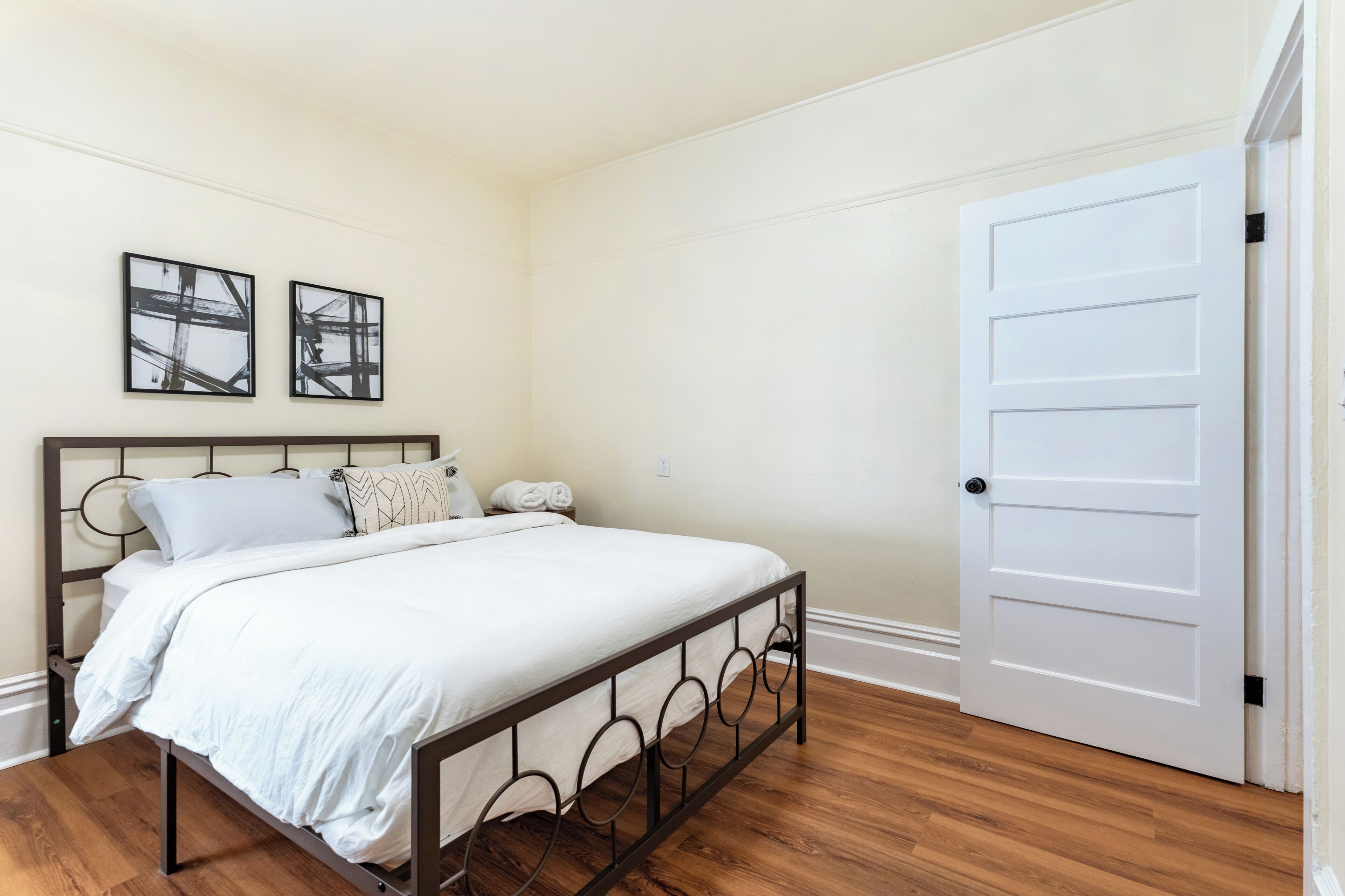 Une chambre à coucher avec un lit, une porte blanche et deux tableaux abstraits accrochés au mur.