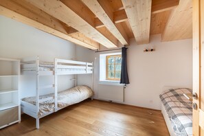 Ein Zimmer mit Etagenbett, einem Fenster mit Vorhängen, einem Heizkörper und einer Tür.