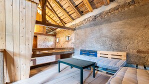A rustic wooden room with a lofted ceiling, a wooden table, a bed with a blue headboard, and a stone wall. - Le Refuge de La Forge - Charmante ferme rénovée (La Forge)