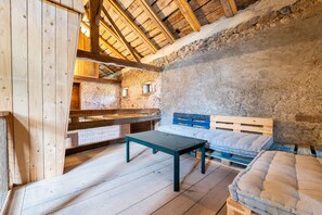 Ein rustikaler Holzraum mit schrägen Decken, einem Holztisch, einem Bett mit blauer Kopfteil und einer Steinwand.