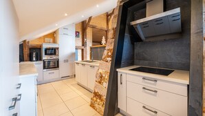 A modern kitchen with built-in appliances, a stone accent wall, and a view of the living area. - Le Refuge de La Forge - Charmante ferme rénovée (La Forge)