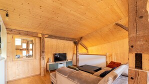 A cozy cabin interior with a wooden ceiling, a sofa, a TV, and a window. - Le Refuge de La Forge - Charmante ferme rénovée (La Forge)