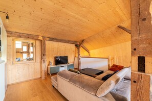 Ein gemütliches Blockhaus-Interieur mit Holzbalkendecke, einer Couch, einem Fernseher und einem Fenster.
