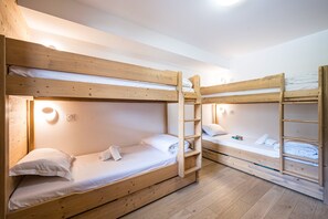 Ein Schlafraum mit Etagenbetten, Holzrahmen, weißer Bettwäsche und einer Leiter.