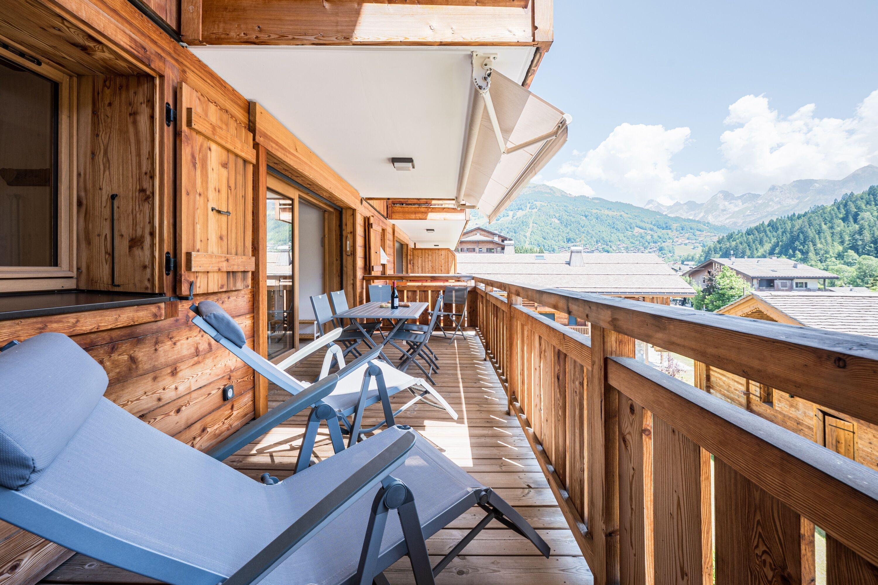 A wooden deck with lounge chairs and a table, overlooking a mountainous landscape.