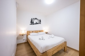 Ein Einzelbett mit Holzrahmen und weißer Bettwäsche, zwei Nachttischlampen und ein Wandbild mit einer Berglandschaft.