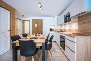 A modern kitchen with white cabinets, a wooden dining table, black chairs, and a built-in oven. - Balcon du soleil n°33 - Balcon avec vue montagne (Le Grand Bornand)