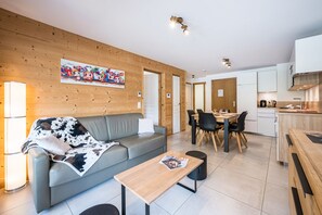 A modern living room with a grey sofa, a wooden coffee table, and a dining area with a wooden table and chairs. - Balcon du soleil n°33 - Balcon avec vue montagne (Le Grand Bornand)