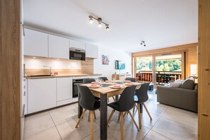 A modern kitchen with white cabinets, a wooden countertop, and a dining area with a table set for four. - Balcon du soleil n°33 - Balcon avec vue montagne (Le Grand Bornand)