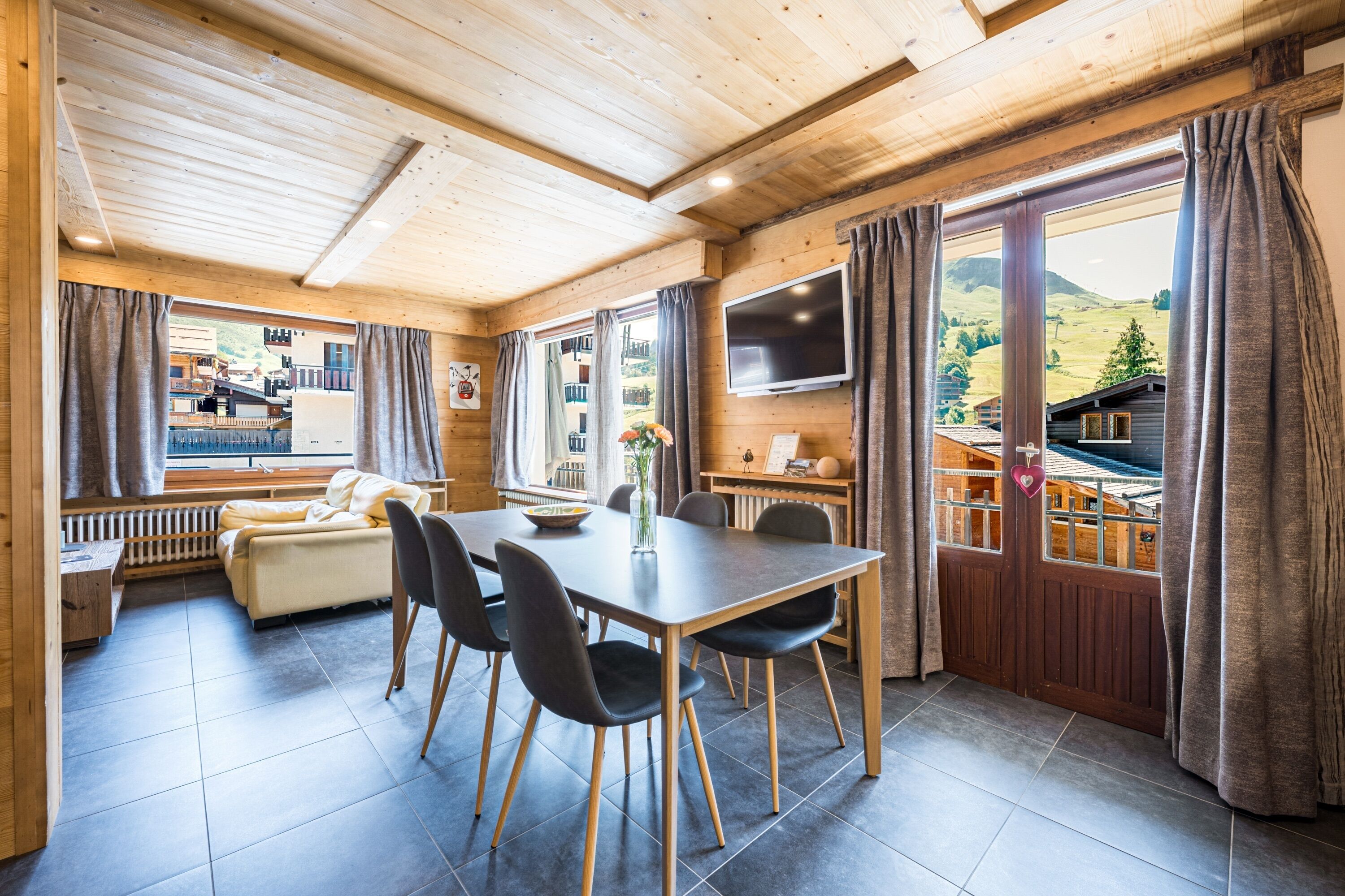 A wooden interior with a dining table, chairs, a sofa, and a TV.