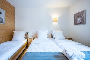 Quarto de hotel com duas camas de solteiro, cabeceira de madeira, luminária fixada na parede e um quadro emoldurado.