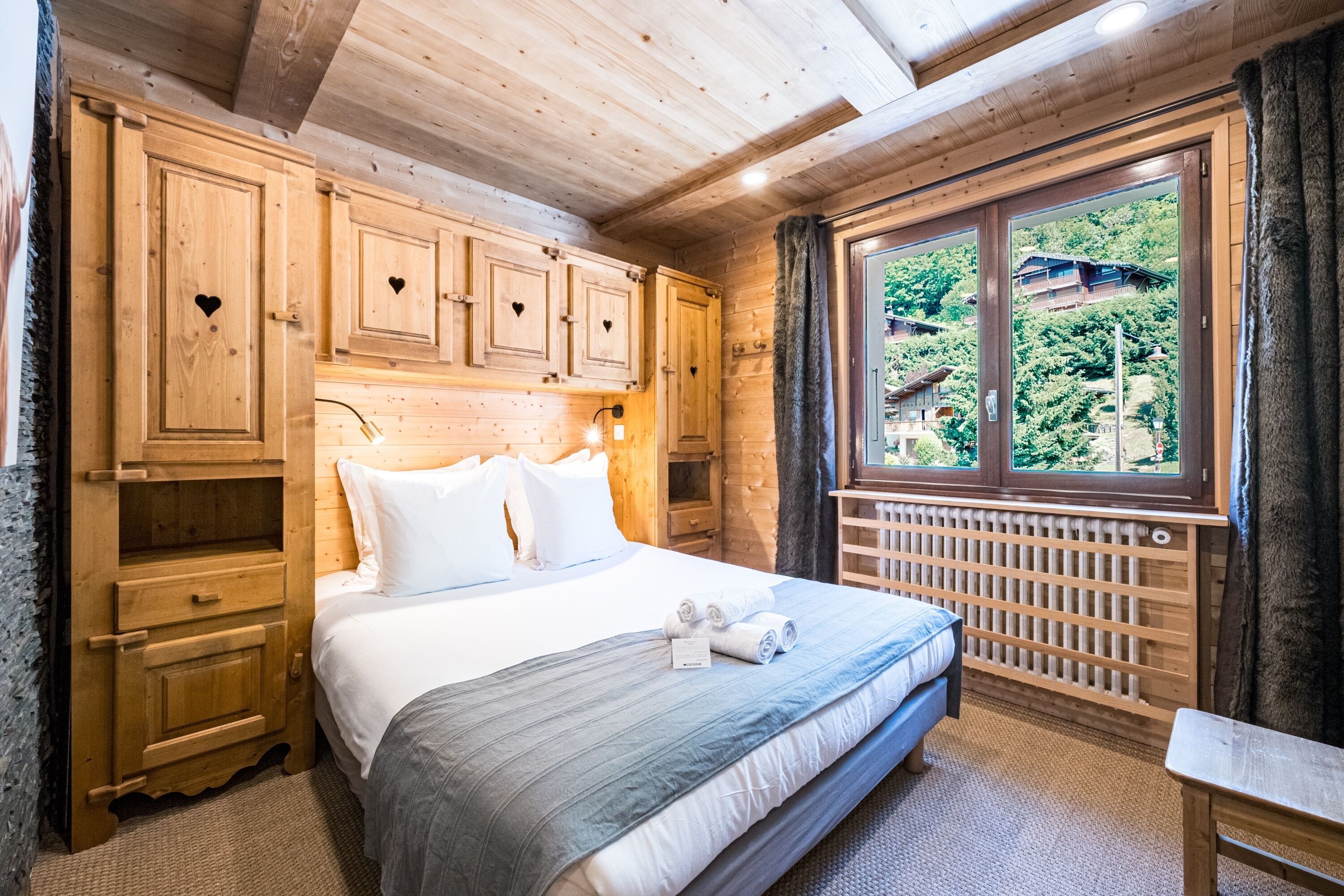 Une pièce en bois avec un lit, des armoires en bois et une fenêtre donnant sur un paysage verdoyant.