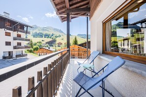 Ein Balkon mit Blick auf eine Berglandschaft, einem Holgitter und zwei blauen Stühlen.