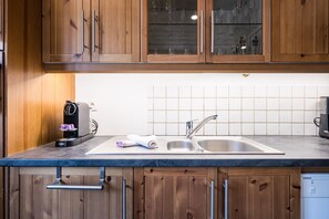 A kitchen with wooden cabinets, a stainless steel sink, and a coffee maker. - Mont Blanc - Apt N°1 (Le Grand Bornand)