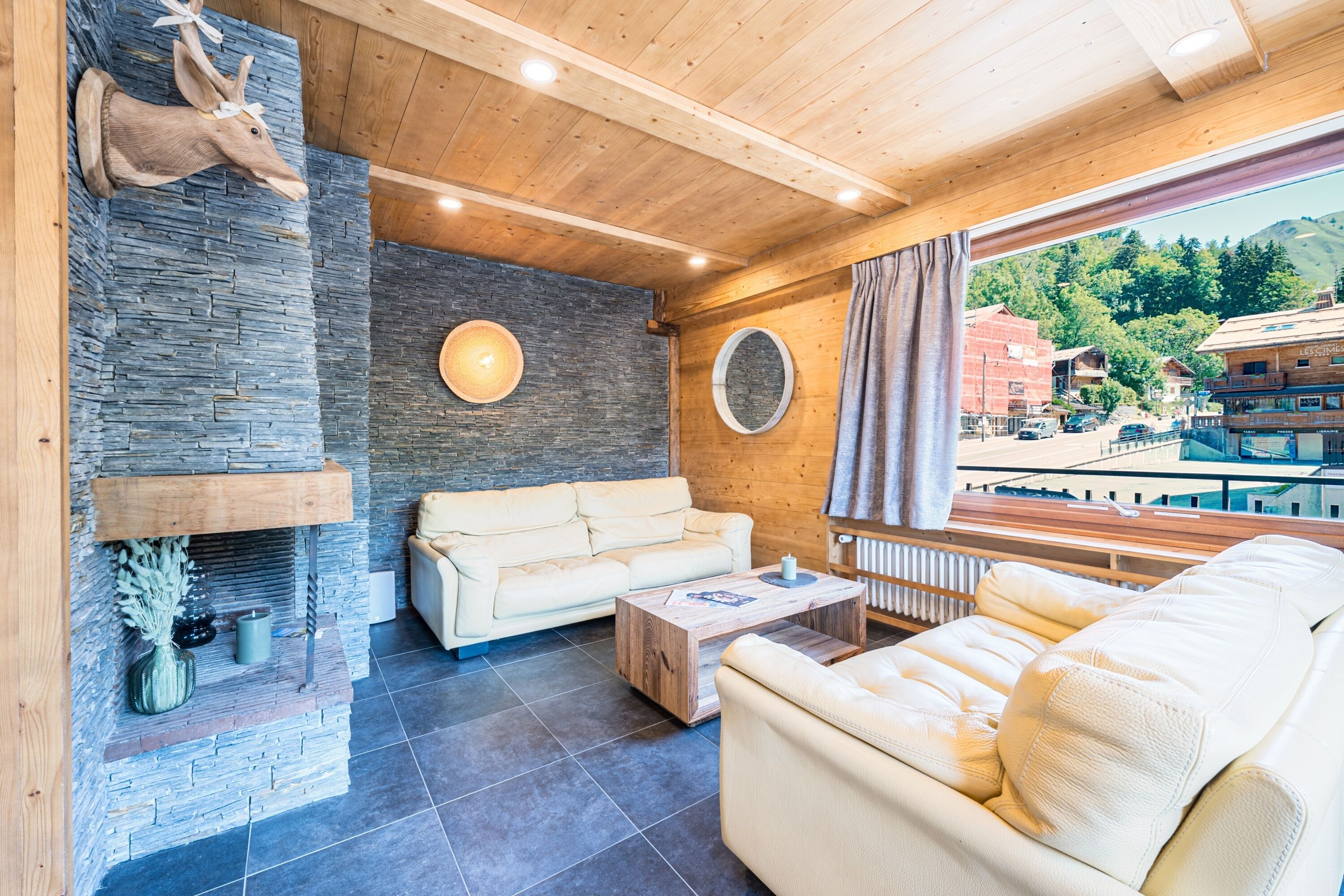 Ein modernes Interieur mit Kamin aus Stein, Ledersofas und Blick auf eine Bergstadt.