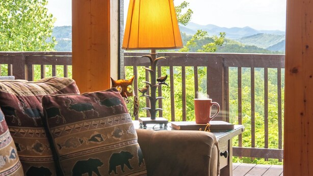 A wooden deck with a sofa, a lamp, and a table with a mug. - Full Arcade Game Room, Hot Tub & Mountain Views, Sleeps 10 Near Dollywood (Sevierville)
