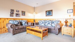 A living room with a wooden paneled wall, a brown leather sofa with patterned cushions, a wooden coffee table, and a wooden nightstand with a lamp. - Full Arcade Game Room, Hot Tub & Mountain Views, Sleeps 10 Near Dollywood (Sevierville)